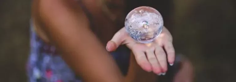 Mano sosteniendo una esfera de cristal transparente.